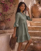 Vestido corto verde militar de lino, con cuello mao, escote en V con botones, mangas tres cuartos acampanadas con volados y falda con volado en el ruedo.