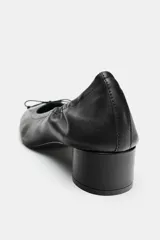 Zapato tipo bailarina de piel color negro, con tacón bloque bajo, puntera redonda y detalle de pequeño lazo en la parte delantera.