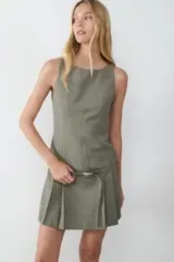 Vestido corto sin mangas color gris verdoso, confeccionado en tejido estructurado. Presenta un escote redondo, diseño ajustado en la parte superior y falda con tablas. Incluye un cinturón fino con hebilla metálica a la altura de la cadera.