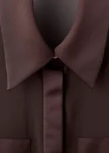 Camisa de tejido semitransparente color marrón oscuro, con cuello camisero, cierre frontal de botones ocultos y mangas largas con puños abotonados.