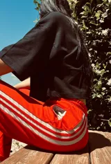 Pantalón deportivo color naranja con las icónicas tres rayas blancas laterales características de la marca Adidas.