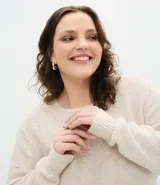 Suéter de punto color beige con cuello redondo, manga larga y aplicaciones de perlas distribuidas por toda la prenda. Presenta puños y ruedo acanalados.