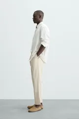 Pantalón de corte relajado color beige confeccionado en tejido de mezcla de algodón y lino. Posee cintura elástica ajustable con cordón, bolsillos frontales y bolsillos traseros de vivo.