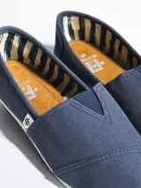 Alpargata de lona negra con suela de goma blanca flexible. Presenta una etiqueta pequeña con el logo de la marca en el lateral y plantilla interior de símil cuero.