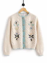 Cardigan de lana merino color marfil, con bordados florales artesanales, trenzas y rombos calados en el frente. Posee cierre frontal con botones vintage dorados y terminaciones en crochet celeste en cuello, puños, ruedo y tira de botones.