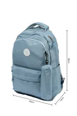 Mochila escolar de tela color azul claro, con múltiples compartimentos con cierre, bolsillo frontal con cierre y un pequeño accesorio colgante cilíndrico a juego. Presenta un parche circular con un emoji sonriente en el frente.