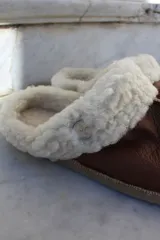 Pantufla de cuero color habano con interior de piel sintética, suela de goma y detalle de costura central.