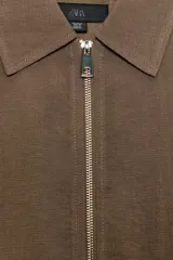 Cazadora tipo bomber color marrón, confeccionada en mezcla de viscosa. Tiene cuello solapa, manga larga, bolsillos de vivo en los laterales y bajo acabado en elástico. Cierre frontal con cremallera metálica.