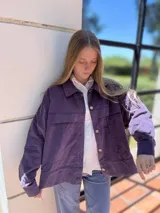 Campera corta de pana color violeta con cuello camisero, cierre frontal con botones dorados, bolsillos de parche en el pecho y corte recto.