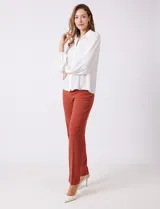 Camisa de gasa blanca con cuello solapa y cierre frontal de botones. Presenta un delicado galón de encaje festoneado a lo largo de la cartera frontal. Sus mangas largas son ligeramente abullonadas, con insertos de puntilla horizontal y puños elásticos fruncidos.