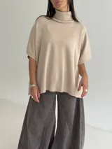 Poncho de tejido de punto color marrón chocolate, con cuello alto tipo polera y mangas cortas amplias. Presenta un diseño holgado con terminaciones acanaladas en el ruedo.