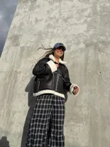 Campera tipo gamulán de cuero sintético negro con interior y detalles de corderito blanco. Presenta cierre frontal, bolsillos laterales y diseño holgado.