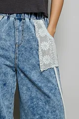 Pantalon de denim azul con lavado vintage, corte ancho y recto, cintura elastizada, grandes bolsillos delanteros de encaje y detalles de ribetes trenzados.