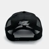 Gorra tipo trucker color negro con panel frontal bordado que presenta el logo 'LA' y diseño de llamas tribales en tonos gris y blanco. Cuenta con parte trasera de malla ajustable.