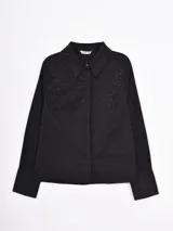 Camisa negra de manga larga con cuello clásico y cierre frontal de botones. El frente de la prenda presenta un delicado detalle de pequeñas tachas o cristales incrustados en la parte superior.