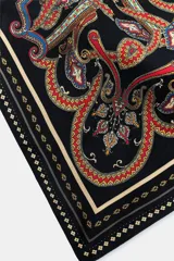 Cinturón tipo pañuelo de tejido satinado con estampado paisley en tonos rojos, azules, verdes y dorados sobre fondo negro. Presenta cierre con hebilla metálica y aplicación de tiras de piel.