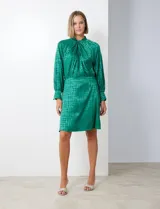 Vestido corto verde esmeralda de gasa laminada con cuello alto entrelazado, manga larga raglán, cintura elastizada y espalda con abertura ojal y botones.