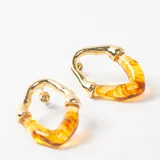 Caravanas de diseño irregular con estructura superior metálica en tono dorado y parte inferior de resina translúcida con efecto marmolado en tonos amarillos y ámbar.