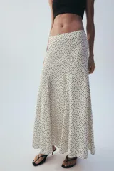 Falda midi fluida de tiro medio en color crudo con estampado de lunares negros, de corte evasé y caída ligera.