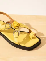 Sandalia baja de cuero vacuno con tiras cruzadas y aplique decorativo. Tiene hebilla en el talón y empeine para regular el calce.