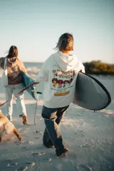 Hoodie color natural con estampado en la espalda con la frase "Glassy Waves" y dibujos de palmeras, labios y tablas de surf.