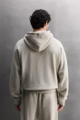 Sudadera con capucha color gris claro, de corte holgado, con bolsillo tipo canguro y cordones ajustables.