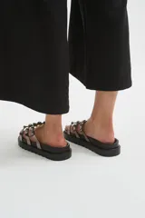 Sandalias chatas de plataforma dentada negra, con múltiples tiras metalizadas decoradas con tachas esféricas brillantes.