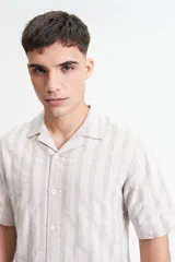 Camisa de manga corta a rayas verticales blancas y grises, con cuello camisero y corte recto. El modelo usa talle M.