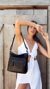 Bandolera de símil cuero color negro con dos bolsillos frontales con cierre, un bolsillo trasero y tres bolsillos internos. Detalles de tachas metálicas y correa larga regulable.