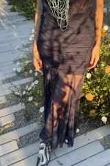 Falda larga de color azul marino confeccionada en microtul y gasa. Presenta un diseño con frunces y plisados en la zona de la cadera que brindan un ajuste al cuerpo, y una parte inferior fluida con transparencias y efecto godet.