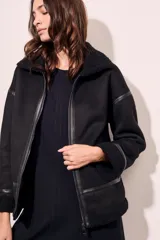Campera tipo gamulán de corte oversize, color negro, con interior y cuello de corderito sintético. Presenta cierre frontal, detalles de costuras y puños con terminación en corderito.