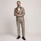 Traje formal de tres piezas en tono tostado brillante, compuesto por saco con solapas en contraste, pantalón de corte recto y chaleco a juego, acompañado de moño.