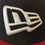 Gorro New Era 59FIFTY negro con visera roja y logo bordado en blanco.