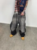 Jean de corte amplio en color negro con efecto acid wash. Presenta cierres laterales metálicos que permiten ajustar la silueta entre corte recto, oxford o baggy. Incluye una estampa gráfica de gran tamaño en la parte trasera con detalles bordados, bolsillos amplios y una etiqueta de cuero legítimo en la cintura.
