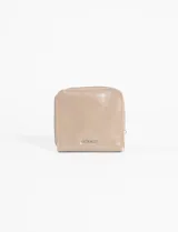 Billetera pequeña de cuero vegano color beige, con cierre perimetral de cremallera y placa metálica con el nombre de la marca en la parte frontal.