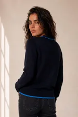 Cardigan de punto azul con ribetes en contraste negro, cuello redondo, cierre frontal con botones y bordado pequeño en el pecho.