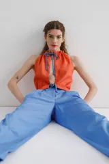 Top sin mangas color naranja, con cuello halter y abertura en el delantero y espalda. Detalle de fruncido en el cuello y ruedo que se ajusta y cierra con lazo en contraste color azul.