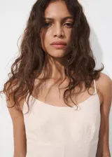 Vestido corto de color beige con diseño fluido, tejido plisado, cuello redondo y tirantes finos ajustables.