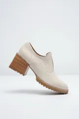 Zapato de cuero color beige, con taco de madera y suela dentada. Presenta un diseño slip-on con detalles de textura en relieve en los laterales y el empeine.