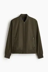 Campera bomber de color verde militar, con cuello elevado acanalado, cierre frontal, bolsillos laterales con cierre y ribetes acanalados en puños y bajo.