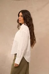 Camisa blanca de manga larga con diseño bordado y calado en patrón de rayas verticales. Posee cuello clásico, cierre frontal con botones y puños anchos.