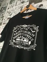 Remera negra de algodón con estampado frontal de una tabla ouija en color blanco.