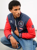 Campera bomber azul marino estilo retro, con cierre frontal de botones a presión, cuello, puños y ruedo con tejido acanalado tricolor. Presenta el logo de Umbro y el escudo del Club Nacional de Football bordados en el pecho, junto con el año 1899 y parches decorativos en las mangas.