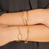 Pulsera de malla metálica con dije central en forma de corazón, ambos en acabado dorado.