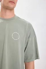 Camiseta verde de corte amplio y recto, con estampado de texto circular en la espalda.