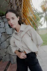 Camisa de algodón color beige con detalles de encaje y broderie en el canesú y las mangas. Presenta cuello camisero, cierre frontal con botones y mangas largas con puños.