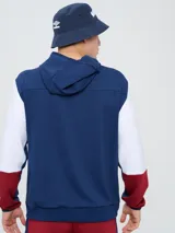 Canguro deportivo Umbro del Club Nacional de Football, modelo Evoque. Diseño con bloques de color blanco en el torso, azul en la capucha, laterales y parte superior de las mangas, y rojo en los puños. Incluye capucha con cordón ajustable, logo de Umbro y escudo del club bordados en el pecho.