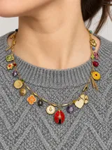 Collar corto de cadena dorada decorado con múltiples dijes y amuletos colgantes, incluyendo una vaquita de san antonio esmaltada en rojo y negro, monedas con relieves, símbolos de trébol, soles, corazones y piedras de colores.