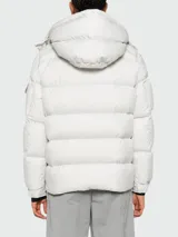 Campera puffer Moncler Maya color gris claro, rellena de plumas, con capucha desmontable, cierre frontal con botones a presión y bolsillos laterales con cierre.