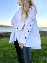 Camisola blanca oversize con cuello camisero, mangas largas con puños abotonados y cierre frontal con botones negros.